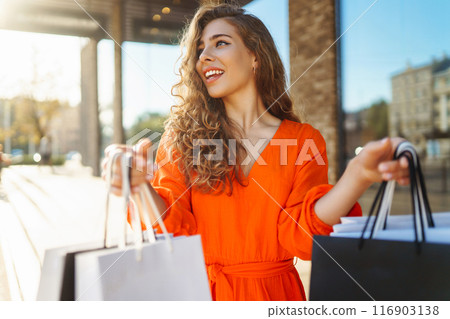 Happy woman with shopping bags walking on sunny street. Concept of lifestyle, buying, selling. Happy woman with shopping bags walking on sunny street. Concept of lifestyle, buying, selling. 116903138