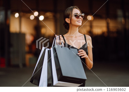 Fashion woman enjoying shopping. Elegant woman wears black dress holding black and white shopping bags. Fashion woman enjoying shopping. Elegant woman wears black dress holding black and white shopping bags. 116903602