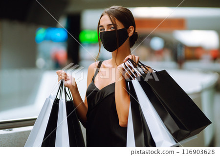 Young woman in protective black medical mask on her face with shopping bags in the mall.Covid-2019. 116903628