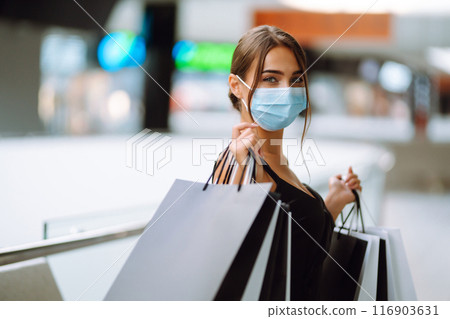 Fashionable woman in protective medical mask with shopping bags walking in the mall. Covid-19. 116903631