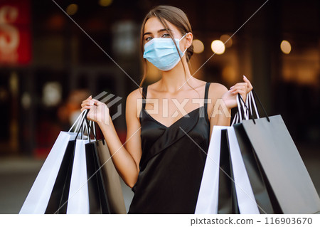 Fashionable woman in protective medical mask with shopping bags walking near mall. Covid-19. 116903670