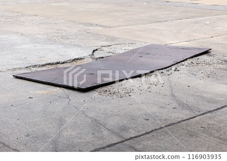 damaged concrete road surface temporary bad poor repair using thick iron sheet to cover cracked cement pavement. 116903935