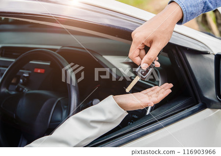 closeup male hand giving a car key to women sitting in the car for healthy car ready to travel safe trip concept. 116903966