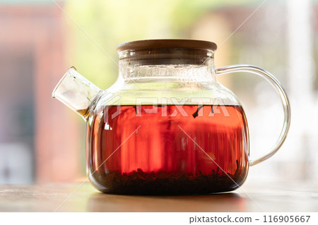 Glass Teapot holding Freshly Brewed Tea on Wooden Table in Sunlight creates a cozy atmosphere 116905667