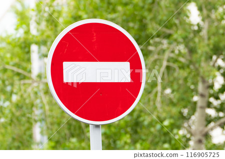 Close-up of a red no entry traffic sign with green foliage background, indicating restricted access 116905725