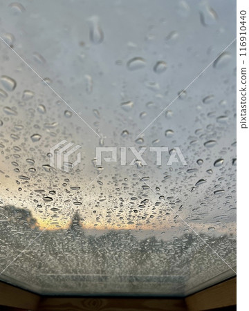 Water drops on the window with a view of the city at sunset landscape. 116910440
