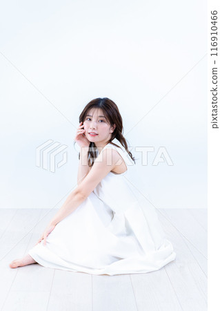 一位身穿白色連身裙的年輕女子坐在地板上 116910466