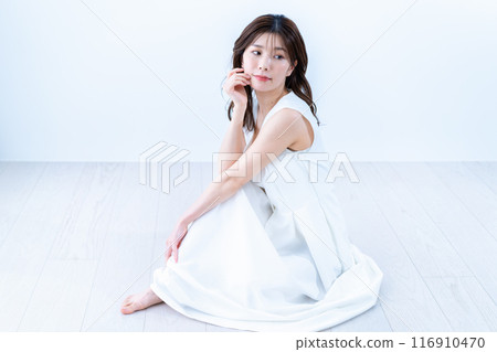 一位身穿白色連身裙的年輕女子坐在地板上 116910470