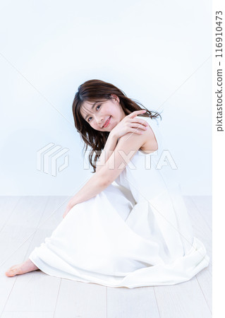一位身穿白色連身裙的年輕女子坐在地板上 116910473