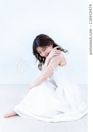 一位身穿白色連身裙的年輕女子坐在地板上 116910474