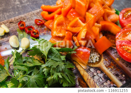 Vegetables and herbs on cutting board. Sliced tomato, bell pepper, chilli pepper, garlic and parsley on the table. Summer salad ingredients. Healthy eating. Organic food background. 116911255
