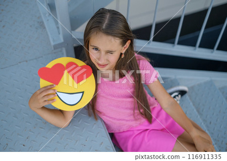 A winking Girl sitting on the stairs shows emojis with loving eyes and big hearts A winking Girl sitting on the stairs shows emojis with loving eyes and big hearts 116911335