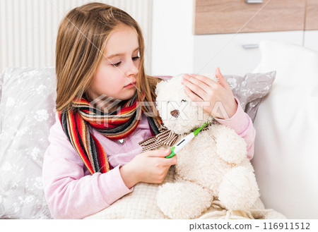 Little ill girl with scarf measuring teddy bear's temperature 116911512