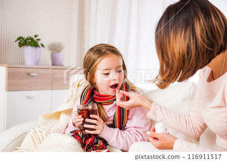 Mum giving pill to ill daughter drinking tea Mum giving pill to ill daughter drinking tea 116911517