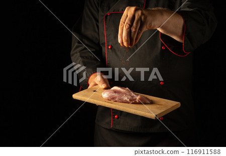 The chef sprinkles dry aromatic spices on the meat steak with his hand before cooking. Hotel or restaurant service concept. Cooking veal The chef sprinkles dry aromatic spices on the meat steak with his hand before cooking. Hotel or restaurant service concept. Cooking veal 116911588