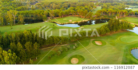 Panorama of golf course at sunset. Scenic panoramic view of golf fairway. Golf field with beautiful pines 116912087
