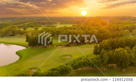 Panorama of amazing golf course at sunset with dramatic sky. Scenic panoramic view of golf fairway with pond. Golf field with beautiful pines 116912088