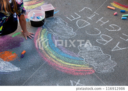 Children draw a rainbow on the asphalt with colored chalk. Sidewalk. 116912986