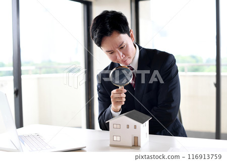 A young man in a suit looking at a model house with a magnifying glass A young man in a suit looking at a model house with a magnifying glass 116913759