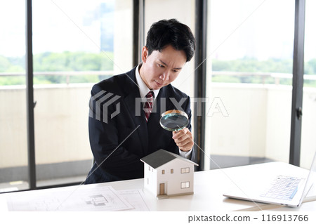 一個穿著西裝的年輕人用放大鏡看著房屋模型 116913766