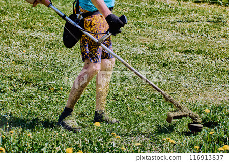 Landscaper legs are covered in shredded grass when he uses weed eater machine without wearing protective clothing. Landscaper legs are covered in shredded grass when he uses weed eater machine without wearing protective clothing. 116913837