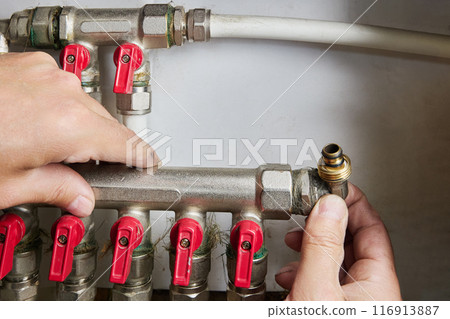 Plumber repairing water distribution collector, pipe manifold with manual control valve in home system of water supply. 116913887