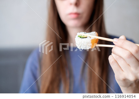 A young woman with long hair holds rolls on sticks against the background of her face, close-up 116914054