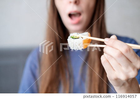 A young woman with long hair holds rolls on sticks against the background of an open mouth, close-up 116914057