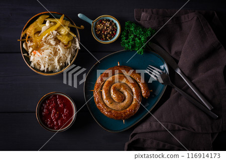 Traditional German dish, Fried spiral sausage, with sauerkraut,with red sauce, on a dark gray wooden background, top view, horizontal, no people, 116914173