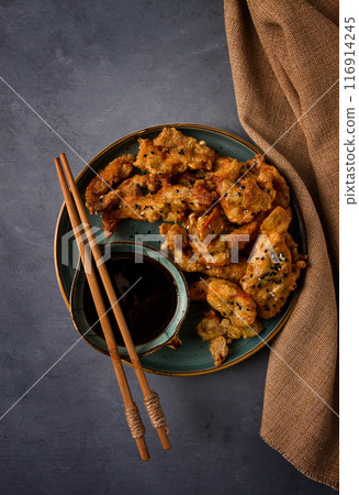 Fried meat in batter, deep-fried, with sesame seeds, and soy sauce, on a gray table, there are no people, 116914245