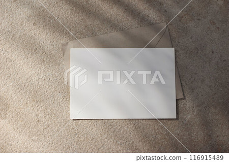 Empty horizontal greeting card invitation mockup, craft envelope. Beige limestone backgound in sunlight. Palm leaf shadow overlay. Modern branding template. Tropical summer, vacation. Flat lay, top 116915489