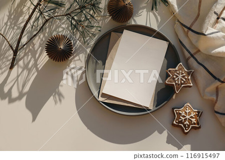 Christmas still life. Empty greeting card, invitation mockup in sunlight. Pine tree branches, christmas balls. White table background. Checkered plaid, gingerbread cookies. Winter banner, flatlay, top 116915497