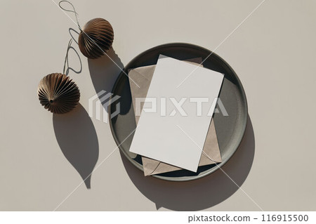 Christmas stationery mockup, ceramic plate. Blank greeting card, invitation template. Craft envelope, brown folded origami Christmas ornaments, balls in sunlight. Beige table background. Flat lay, top 116915500