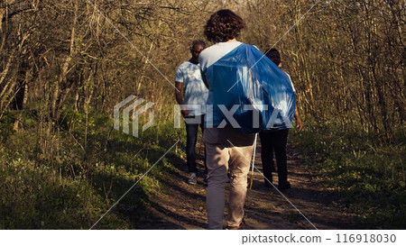 Satisfied people leaving the woods after a productive litter cleanup session, being successful in cleaning the forest environment from junk and plastic waste. Happy proud activists. Camera B. Satisfied people leaving the woods after a productive litter cleanup session, being successful in cleaning the forest environment from junk and plastic waste. Happy proud activists. Camera B. 116918030