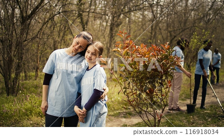 Portrait of mother and daughter volunteering to clean up a forest area, showing a sense of devotion and responsibility for the natural environment conservation. Ecological justice. Camera B. 116918034