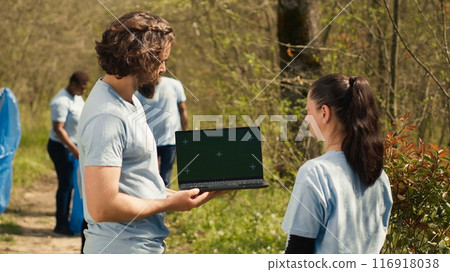 Team of climate and nature activists using laptop with greenscreen near a forest, volunteering to pick up trash and plant trees for future generations. Environmental protection. Camera A. 116918038