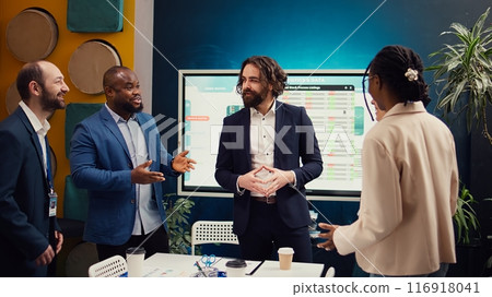 Team of startup employees gathering for a briefing session in boardroom, developing strategies to improve corporate culture and personnel engagement in multiple projects. Camera B. 116918041