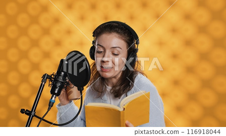 Voice actor reads book while enjoying coffee, recording audiobook using microphone, studio background. Woman using mic and headphones to produce digital recording of novel, drinking beverage, camera A Voice actor reads book while enjoying coffee, recording audiobook using microphone, studio background. Woman using mic and headphones to produce digital recording of novel, drinking beverage, camera A 116918044