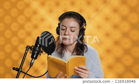 Narrator wearing headphones, reading aloud from book into microphone, exhaling after finally finishing job. Person recording audiobook, creating engaging media content for listeners, camera A 116918046