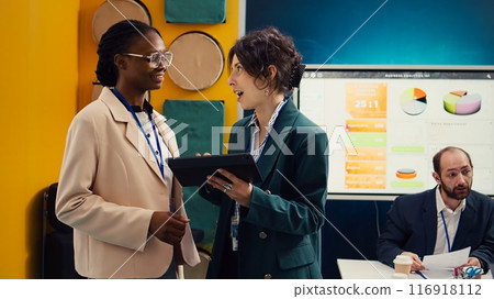 Project manager sharing insight about a new strategy with the new employee, shaking hands and welcoming her to the team in conference room. Coworkers in a new hire introductions meeting. Camera B. Project manager sharing insight about a new strategy with the new employee, shaking hands and welcoming her to the team in conference room. Coworkers in a new hire introductions meeting. Camera B. 116918112