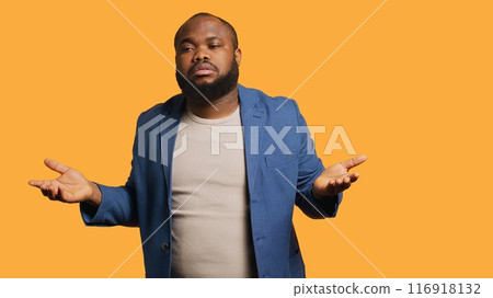 African american man shrugging shoulders, not caring, having detached apathy facial expression. Apathetic BIPOC person doing disinterest indifferent hand gesturing, studio background, camera A 116918132