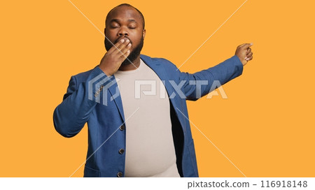 African american man feeling exhausted and yawning, covering his mouth, isolated over studio background. BIPOC person being sleepy during morning, awaken too early, showing sleepiness, camera A African american man feeling exhausted and yawning, covering his mouth, isolated over studio background. BIPOC person being sleepy during morning, awaken too early, showing sleepiness, camera A 116918148
