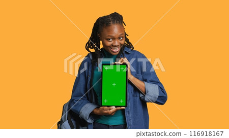 Smiling african american woman presenting tablet with green screen display, isolated over studio background. Cheerful BIPOC person creating promotion with chroma key device, camera A Smiling african american woman presenting tablet with green screen display, isolated over studio background. Cheerful BIPOC person creating promotion with chroma key device, camera A 116918167