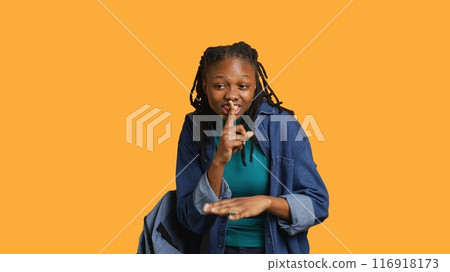 Stern african american woman doing shushing hand gesturing, irritated by noise, having negative mood. Girl placing finger on lips, doing quiet sign gesture, studio background, camera A 116918173