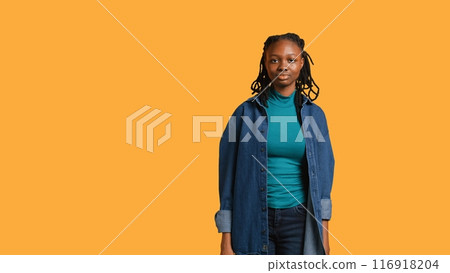 Carefree african american young girl having positive wellbeing, feeling joyful, isolated over studio background. Portrait of pleased woman standing proud, feeling confident, camera B Carefree african american young girl having positive wellbeing, feeling joyful, isolated over studio background. Portrait of pleased woman standing proud, feeling confident, camera B 116918204