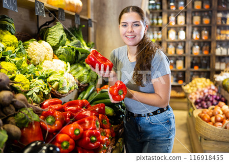 Woman picking out red bell peppers to buy in fruit and vegetables aisle of supermarket 116918455