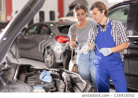 Female customer discussing engine repairs with experienced mechanic in workshop Female customer discussing engine repairs with experienced mechanic in workshop 116918502