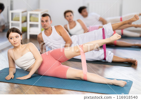 Young girl practicing leg lift with band on knees lying on the side 116918540