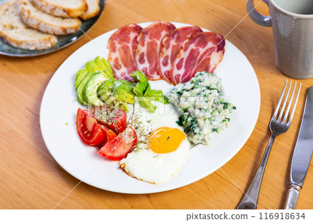American breakfast includes fried egg,pork bacon,tomato slices and avocado,supplemented with bread 116918634