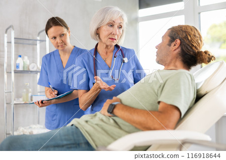 Man sitting in chair and carefully answers mature female doctor questions about well-being 116918644